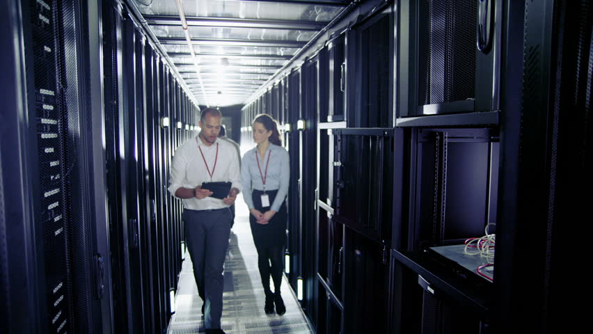 Team of people working in a data center with rows of server racks and super computers. They are looking into data cabinets and checking cables and other equipment.