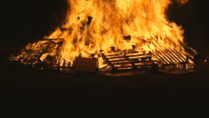 Fire from a big burning campfire, with high flames. The flame pit is made of old wooden branches, the crackling trail is smooth over the dark black night. Real footage. The pyre is almost collapsing.