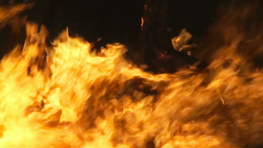 Fire from a big burning campfire, high flames. The flame pit is made of old wooden branches, the crackling trail is smooth over the dark black night. Real footage. The strong wind bends the flames.
