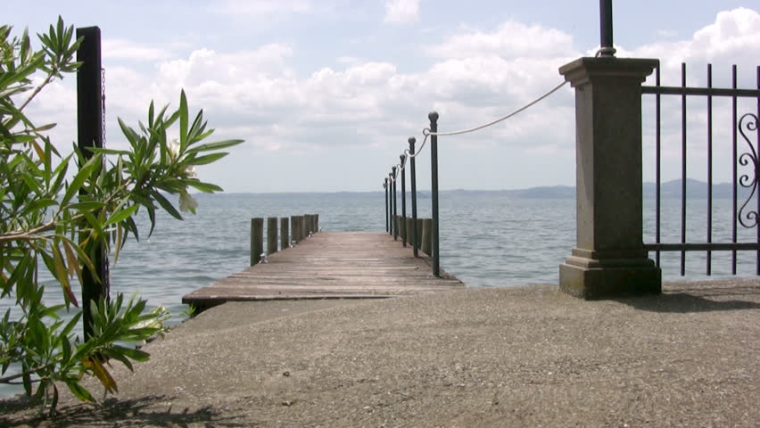 A small lake. Sunny weather. Beautiful clouds in the sky. The view from the shore to empty wooden dock for boats. On calm water, wobble red buoys