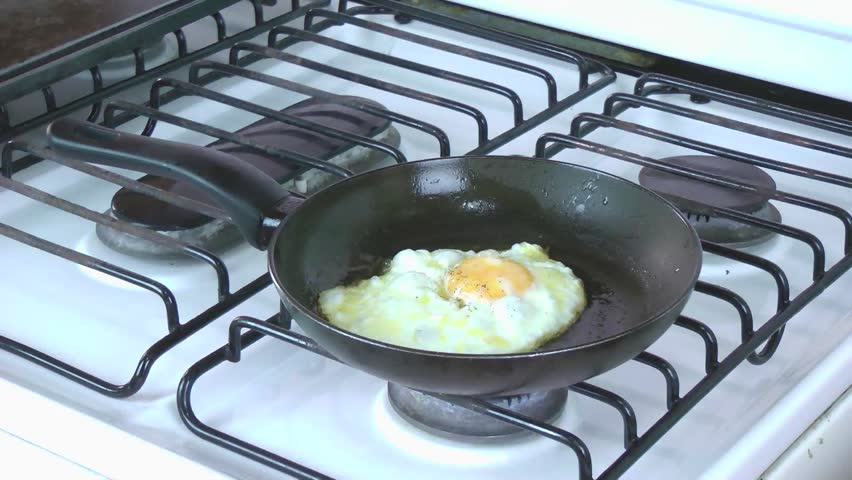 Fried Egg in a Pan. Cooker takes out the egg from the pan and serve it on a plate. 