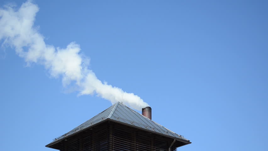 white smoke fume vapour rise from small house building roof chimney on background of blue sky.