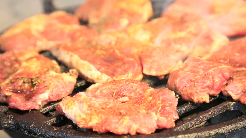 Pork, chicken and beef steaks on barbecue grill in warm tones