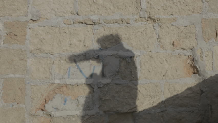 A shadow of a man fights imaginary enemies on a brick wall.