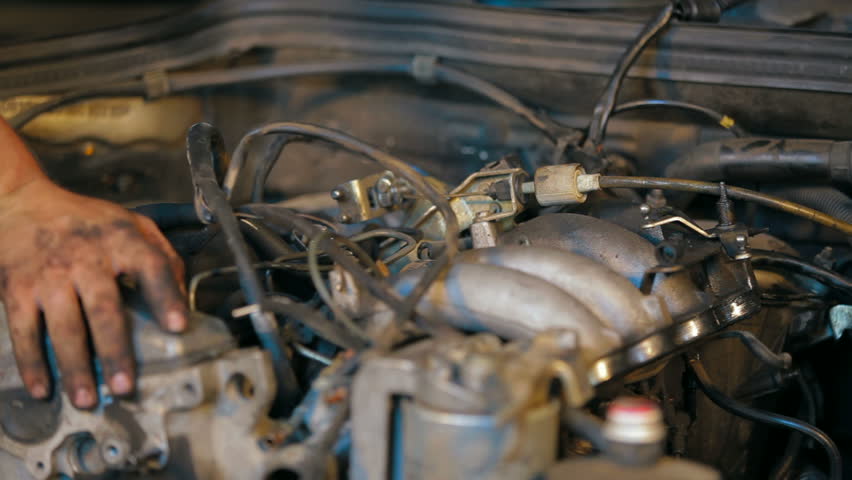Mechanic is dismantling car engine, twisting off the screws.