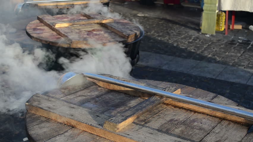 Hot drink wine boil in huge pots and smoke vapour rise in spring outside fair. Ladle with long handle.