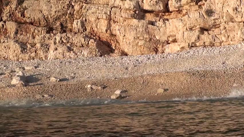 Cliffy beach view from the sea â sunset, waves washing pebbles