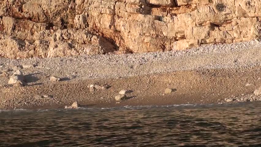Cliffy beach view from the sea â sunset, waves washing pebbles