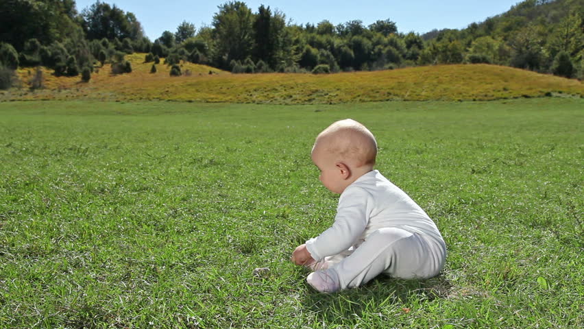 Baby sitting on green lawn and picking up grass