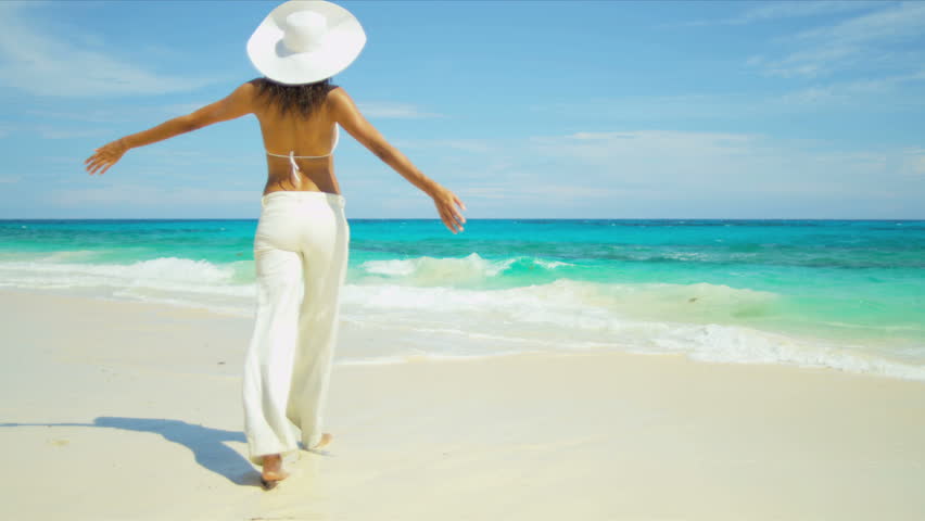 Young girl in bikini top trousers walking alone by ocean on remote island beach shot on RED EPIC