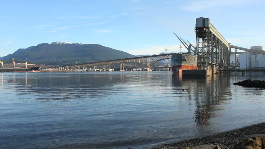 A freighter is loaded with grain at a grain terminal on the shore of Burrard Inlet. The Iron Workers Memorial Bridge between Vancouver and North Vancouver in the background. British Columbia, Canada.
