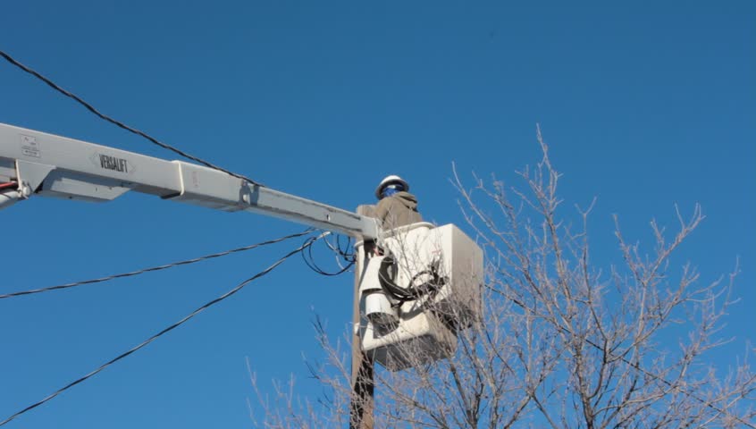 Cable, power, or phone repair man works on cables near a utility pole.