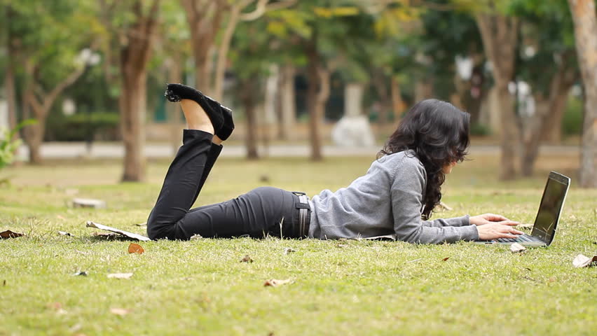 female is typing on the laptop in the park