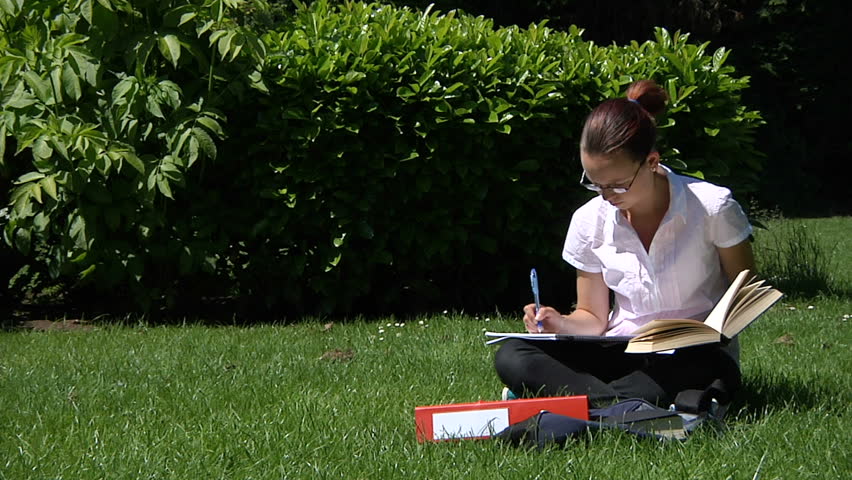 A student studying outdoors with textbook and folders