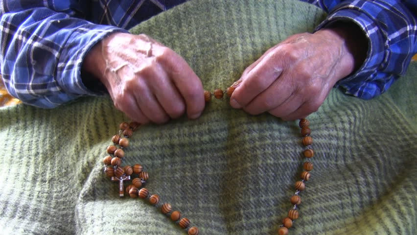 Old wrinkled skin hands hold wooden handmade christian rosary and shaking probably because of Parkinson's disease
