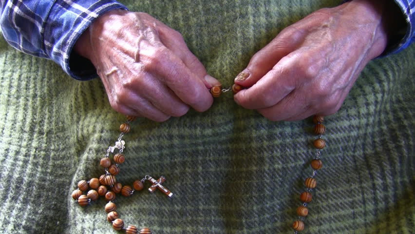 Old wrinkled skin hands hold wooden handmade christian rosary and moving beads slowly