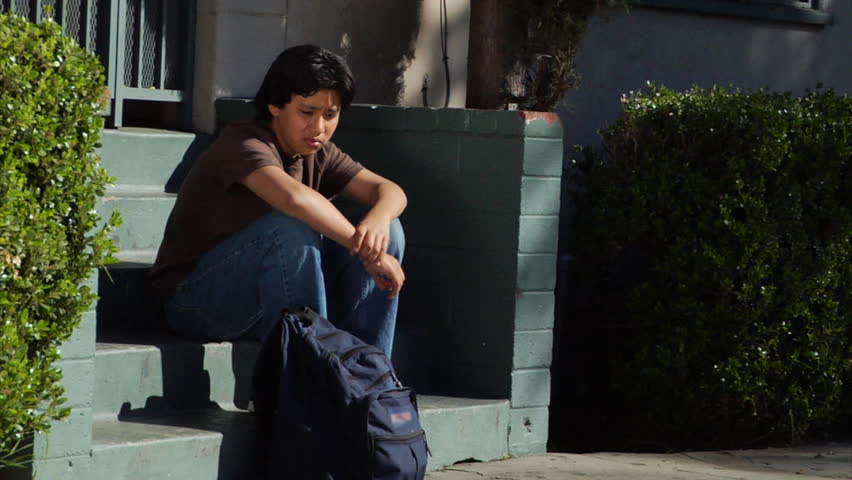 A teenage boy sits on some steps.  He looks around and seems to be frustrated or annoyed about something.