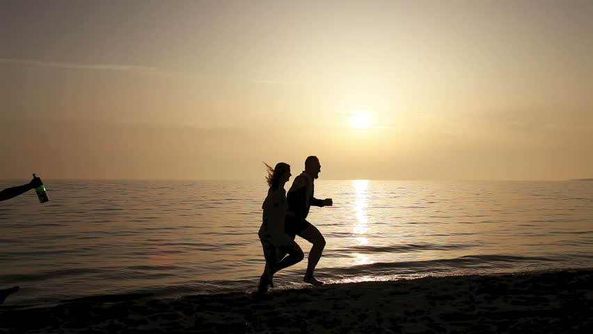 Drunk guy with bottle of champagne running after loving couple at the sea beach
