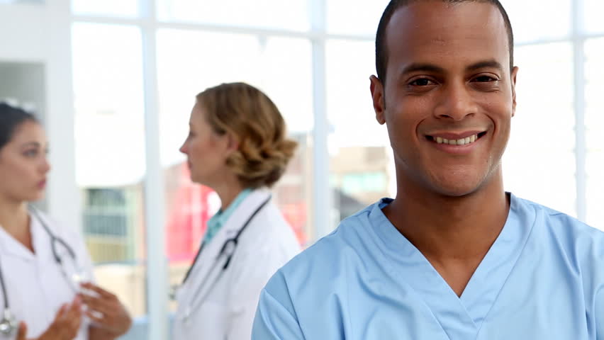 Nurse smiling and standing in front of speaking medical team