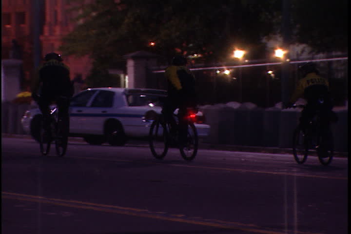WASHINGTON, D.C. - OCTOBER 17, 2001: MS three police officers ride bicycles down Pennsylvania avenue at night, passing tourists and White House.