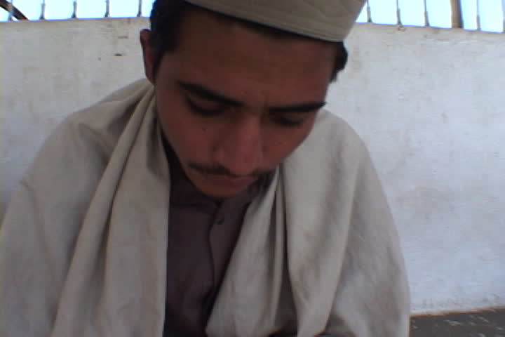 PESHAWAR, PAKISTAN - NOVEMBER 01, 2001: Camera pans left over row of boys in Muslim dress rocking back and forth as they read the Koran.