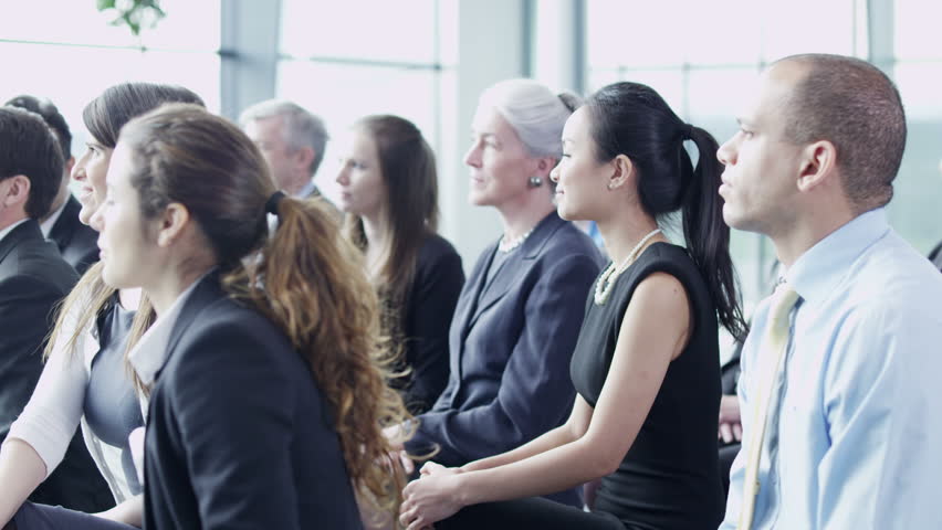 A multi ethnic group of business people of mixed ages are listening to a presentation at a business seminar and asking questions. 