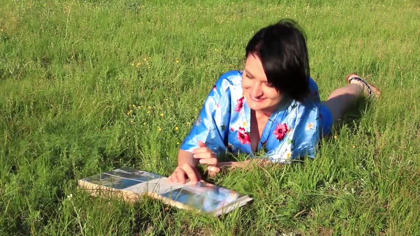 Girl with photo album lying on the green grass