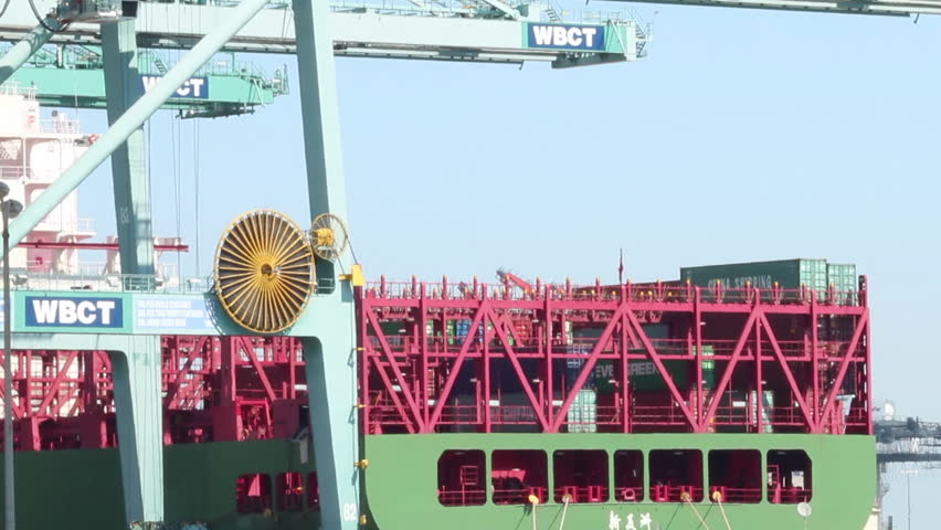 A large gantry crane lifts a shipping container from lower deck on container ship.