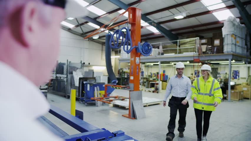 Male and female warehouse or factory workers, in high visibility clothing and hard hats take instructions from their manager.
