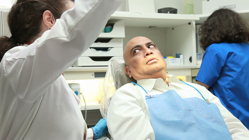 A dentist turns from listening to the dental hygienist consult with a young patient and smiles for the camera.