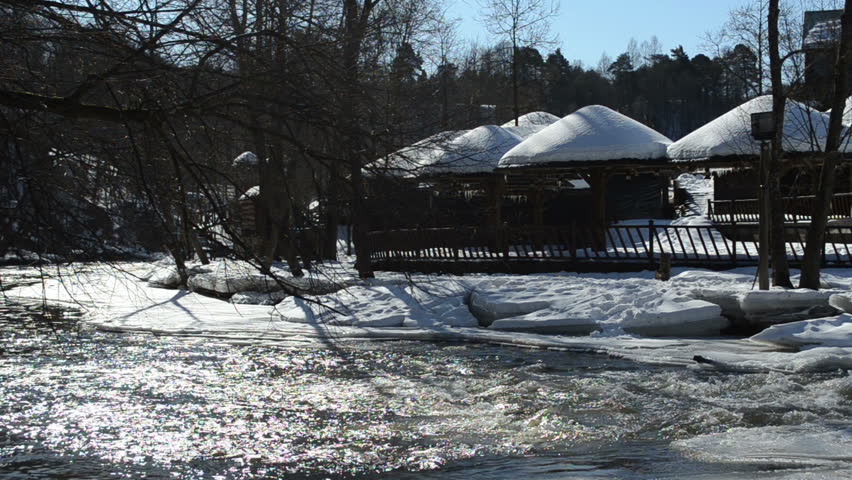 summer recreational houses cottage covered with snow near rapid frozen river in winter.