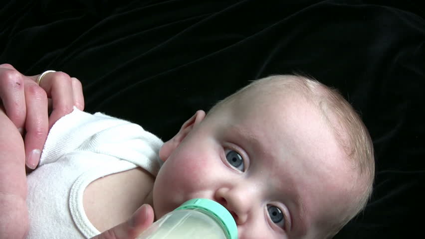 Baby drinking from a bottle, with black background.  HD 1080i