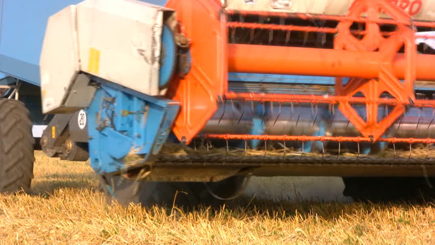 Bright, rotating machinery combine, making the turn onto the field during harvest. Close-up