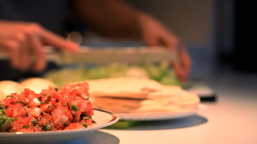 Focus on salsa and guacamole with a person out of focus in the background, preparing a Mexican meal. (Shallow DOF).