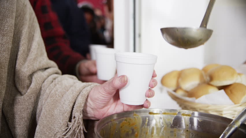 Close up of hands holding up polystyrene cups, eager to take some soup and bread. No faces can be seen. In slow motion.