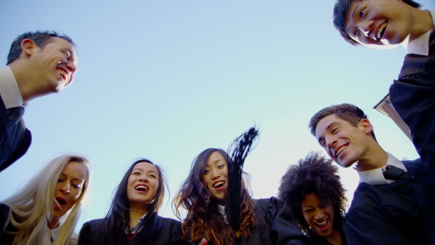 Graduation caps are tossed into the air by a happy group of friends on a bright sunny day. In slow motion. 