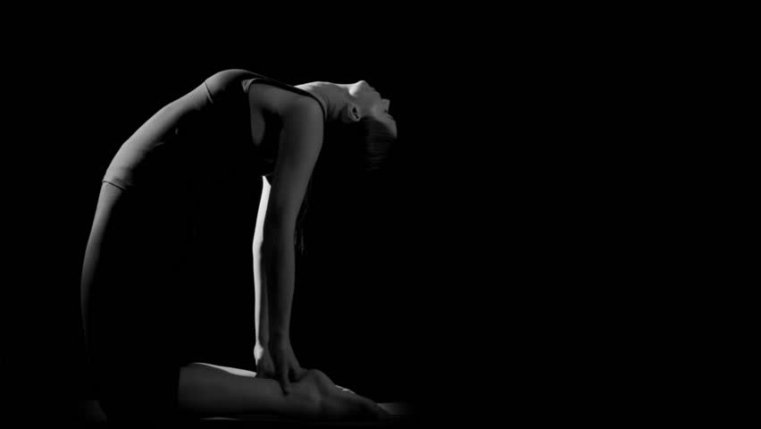 Flexible gymnast stretching backwards against black background. Black and white. Slow motion.