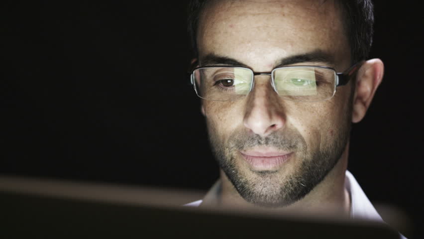 Close up of young man reading his tablet in the dark. Black background. 