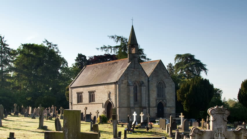 Zoom out from an old stone church in Shropshire in England to show the old grave markings and crosses in the surrounding graveyard