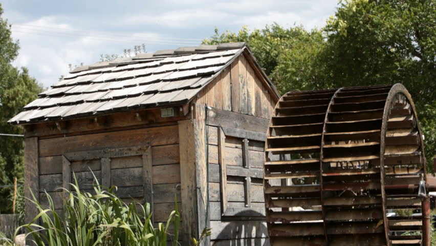 An old antique water wheel turning against a wood building. Turning very fast. Steel wheel and spokes. Turning from power of a small creek in central Utah. Used for a mill.