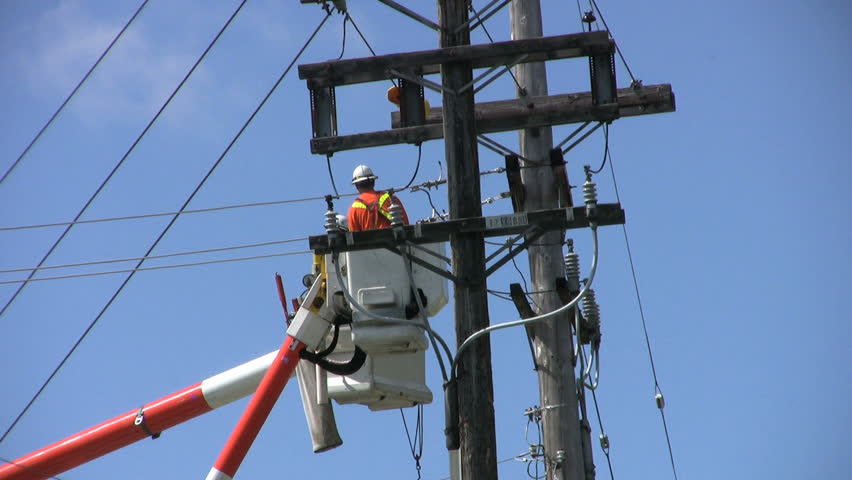 A hydro repair team of two men in orange jumpsuits and hard hats repair a problem on the line.