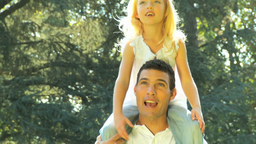 Young father holding his daughter on his shoulders while outdoors on a summers day