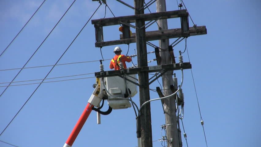 A hydro repair man in an orange jumpsuit and hard hat repairs a problem on the line. 
