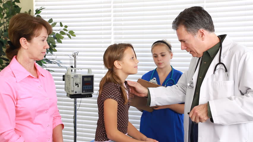A nurse takes notes and a grandmother looks on, as doctor checks a young patients throat and breathing.