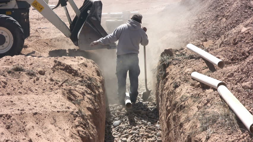 A man works with a shovel removing stones from the bucket of a backhoe for a new septic system.