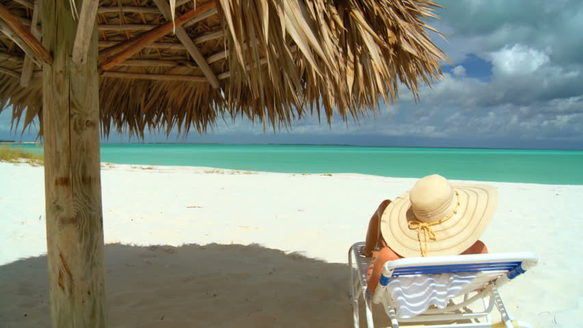 Elegant young female relaxing on white sandy beach looking at aquamarine waters