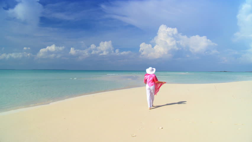 Elegant young female walking on a beautiful white sandy beach looking at aquamarine waters