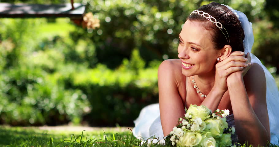Beautiful bride smiling at camera lying on the grass on her wedding day