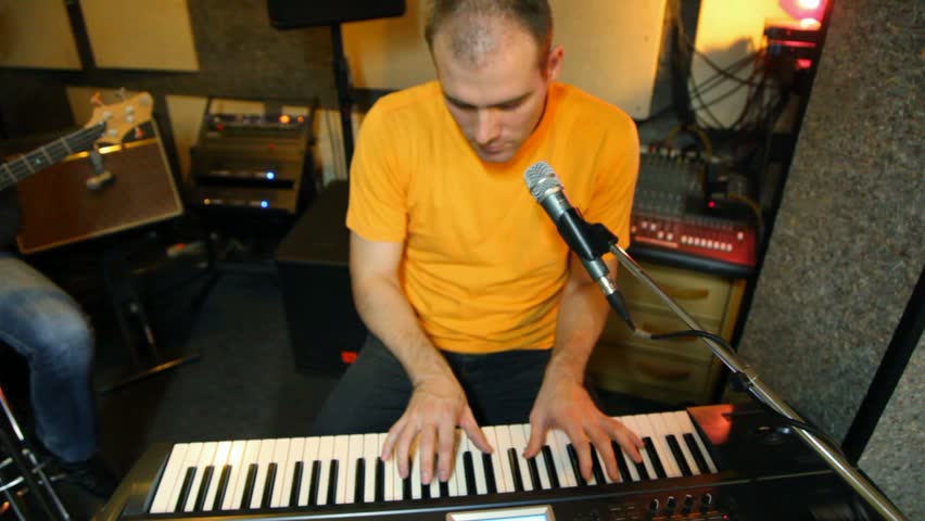 yellow T-shirted keyboard player playing on synthesizer in studio 