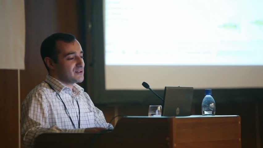 portrait of men speaking through a microphone in dark conference hall 